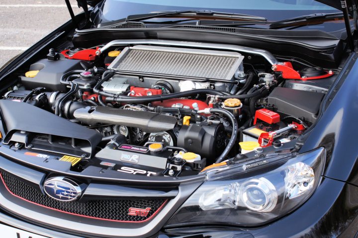 Show off your Subaru!! - Page 9 - Subaru - PistonHeads - The image depicts the front side of a car's open hood. The engine bay reveals a complex assembly of mechanical components, wires, and hoses, characteristic of a modern automotive engine. Notably, there's a prominent red element, possibly a cover or a specific component, situated towards the top of the engine. A few loose objects or parts are scattered around the engine compartment, suggesting it might be a work in progress or under maintenance. The vehicle appears to be a European model, as hinted by the? that is part of the emblem on the grille.