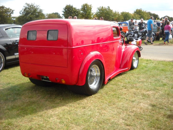 Anyone going to the NASC 40th Nats at Trinity Park? - Page 1 - East Anglia - PistonHeads - In the image, a vibrant red vintage truck is the focal point, parked on a grassy area surrounded by other vehicles. The truck's sleek design and vibrant color make it stand out. In the background, a group of people can be seen, likely spectators or participants of an event where the truck and other vehicles might be on display. The presence of a motorcycle distinguishes the event as possibly having elements of a motor show or exhibition. The vehicles, coupled with the people, indicate a gathering or exhibition of classic or vintage vehicles.