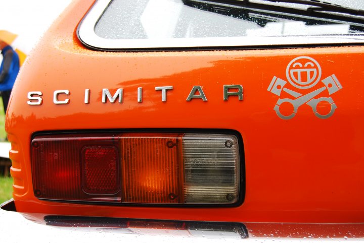 A close up of a school bus on a street - Pistonheads - The image features the rear of a brightly colored car, specifically a Scimitar. The primary focus is the orange rear section of the vehicle, which stands out vividly. On this section, the word "Scimitar" is inscribed in large, capitalized letters. Below the text, a logo or symbol is present, though its specific nature is not clearly visible due to the resolution and angle. The car appears to be outdoors, as evidenced by the hint of a green surface and a sky in the background, albeit not clearly visible. The surrounding area is not distinctly visible, adding to the sense of the car being the primary subject of the image.