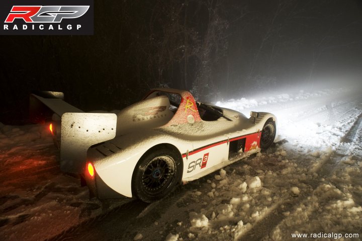 A red fire hydrant sitting on the side of a road - Pistonheads - The image depicts a Radical RGP sports car parked on a stony surface with snow on the ground and trees in the background. The car is red and white with the number 9 prominently displayed on the rear. The lighting suggests it might be early morning or evening due to the shadows and diffused light surrounding the vehicle. The watermark "RADICALALGP" indicates the sponsorship or ownership of the car.