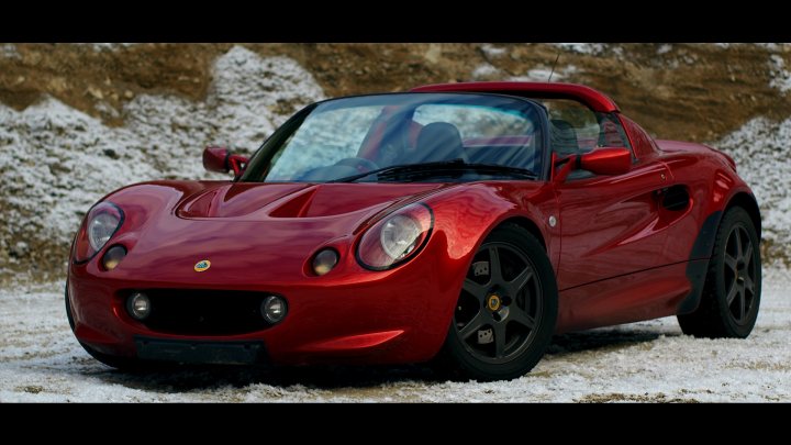 Hiya from Germany - Page 1 - Elise/Exige/Europa/340R - PistonHeads - The image features a bright red sports car that stands out against the backdrop of white snow. The car is parked on a patch of snow-covered ground, which is contrasted by dirt patches visible at the edges of the image. The vehicle's sleek design indicates it's a performance model, with a long hood and short tail typically associated with sports cars. The car's position, turned slightly to the viewer's left, gives a clear view of its front and hood, as well as one of its wheels. The red of the car is striking, adding to its presence in the image.