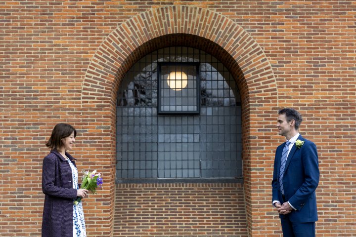 Critical opinions sought  - Page 1 - Photography & Video - PistonHeads UK - The image captures a heartfelt moment between a bride and groom standing in front of a brown brick building with an archway. They are both dressed in formal attire, indicating a special occasion such as a wedding. The man is holding a bouquet of flowers, perhaps preparing to present them to the woman, a common gesture during weddings. The woman's gaze is directed towards something off-frame, possibly drawing her attention to an event or person not visible in the photo. The building behind them appears to be made of brick and has an old-fashioned aesthetic with a street lamp mounted on the wall.