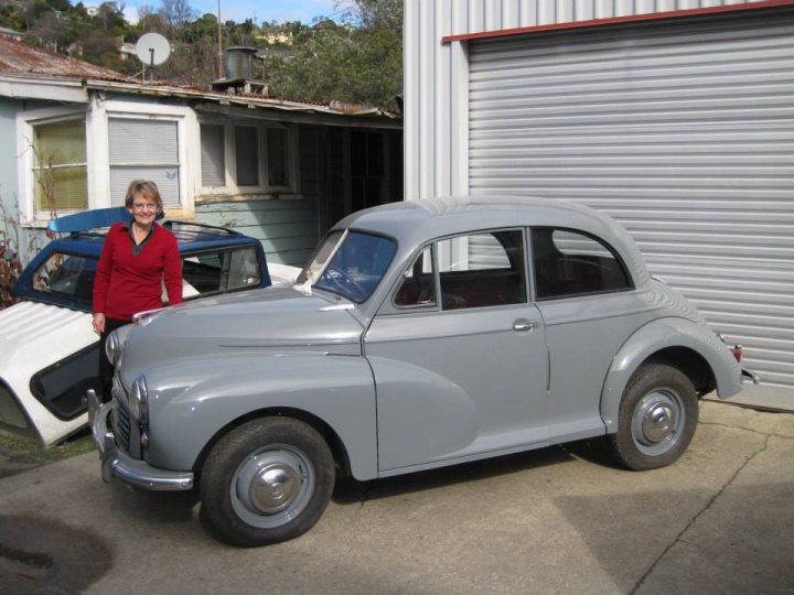 Pistonheads - The image captures a vintage car in a garage setting, with one person standing on the left side. The car, a model likely from the early to mid-20th century, features a distinctive rounded shape, a closed hood, and white-walled rims. It is parked next to a white garage door. The person standing near the car appears to be admiring or assessing it. In the background, there's a glimpse of another vehicle, possibly a truck or a smaller car, partially visible. The atmosphere suggests a vintage vehicle enthusiast might be inspecting or sharing their passion for classic cars.