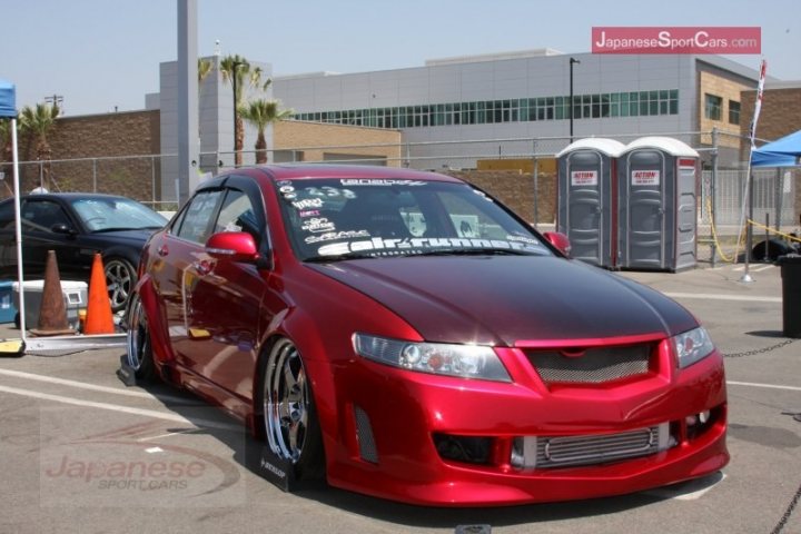 Pictures of decently Modified cars [Vol. 2] - Page 17 - General Gassing - PistonHeads - In the image, a vibrant red Toyota AE85 Lancer is prominently displayed, occupying a large portion of the frame. It is parked on a concrete lot, next to a black car. The Lancer stands out with its customized appearance, featuring silver rims, modified hood, and shiny chrome accents. The vehicle is adorned with various decals, giving it a personalized look. The setting suggests that this might be a car show or an event for enthusiasts, as indicated by the background with tents and other cars. There are also construction cones visible, possibly indicating a temporary parking area.