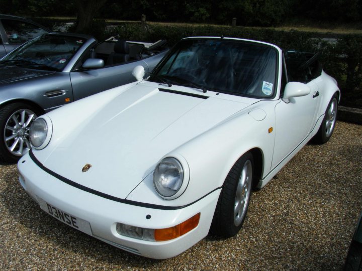 Breakfast Meeting, The Hare, Roxwell 4th June - Page 1 - Kent & Essex - PistonHeads - This image features a vintage sports car, which appears to be a Porsche 914, positioned outdoors. The car is mostly white with a black foreground stripe, and the wheels have a classic multi-spoke design. It is parked alongside another vehicle, possibly a vintage BMW, as indicated by the partial view in the background. The setting seems to be a gravel lot, with the car low to the ground, suggesting an angle to the photograph that emphasizes the car's sleek design.