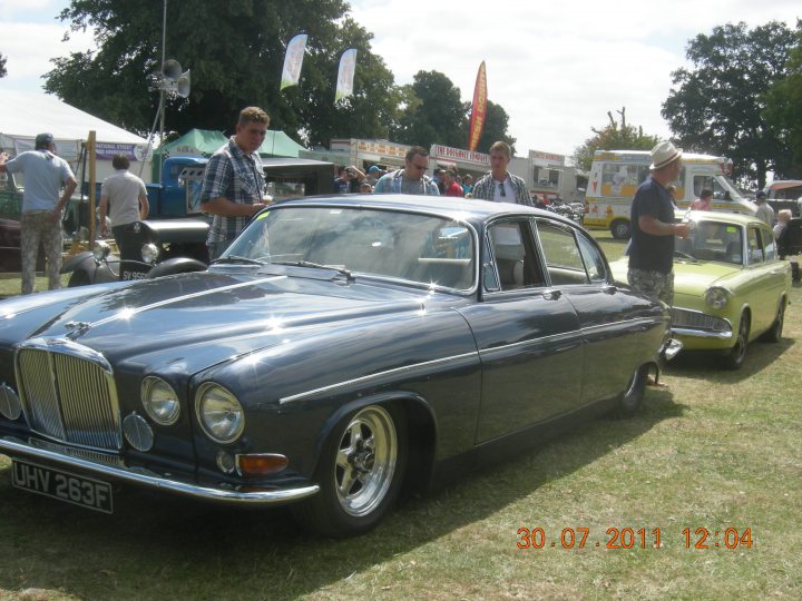 Lowered Jaguar MK10 (?) spotted in Billericay - Page 1 - Kent & Essex - PistonHeads - The image features a vintage blue Bentley resting on a grassy field, surrounded by a gathering of people. Several people are seen standing and chatting near the car, enjoying the car show atmosphere. The bentley's sleek lines and chrome detailing are evident. In the background, other vintage vehicles contribute to the nostalgic vibe of the scene.