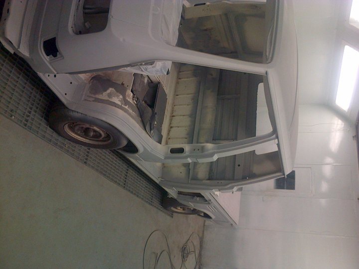 Local gararge space? - Page 1 - South Wales - PistonHeads - The image showcases an in-progress scene in a garage where a white vehicle, specifically a van, is being restored. The van's side has been removed, exposing the door, door handle, and underlying framework. The interior of the van is visible, indicating a floor built into a ramp. The vehicle appears to be in the early stages of the restoration process. Considering the absence of an engine and the missing components in the photo, it is clear that the van is in the process of being transformed.