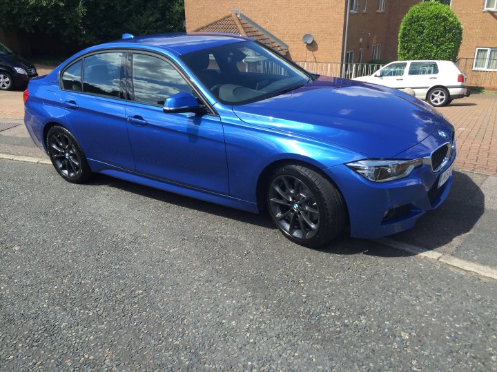 BMW 330e ordered... - Page 220 - EV and Alternative Fuels - PistonHeads - The image shows a shiny blue BMW car parked on a street near the curb. The car is positioned facing towards the right side of the image. The BMW is sleek and finished with a reflective coat, suggesting it might be a newer model. The street is lined with houses, indicating a residential neighborhood. The sky above suggests it might be a cloudy day.