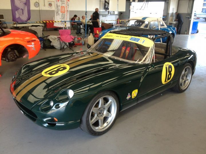 GT style racer hard top - Page 1 - Major Mods - PistonHeads - The image captures a scene from a car show or exhibition. A striking green racer with a gold stripe is parked indoors, its design and colors suggest a vintage racing element. It's prominently displayed behind a protective glass cover. The background is bustling with activity, featuring a display of other cars and a collection of people milling around, possibly attendees or staff of the event. A signage can be seen with the number "18" and the word "Racer," further emphasizing the theme of the motorsport exhibition. The overall atmosphere is vibrant, with a sense of excitement and admiration for the automotive world reflected in the gathering and the time taken to restore and maintain the cars on display.