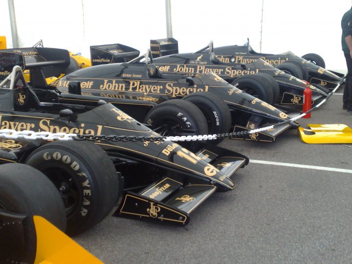 Pistonheads Snetterton - The image shows a collection of race cars exhibited in a line on what appears to be a race track or similar location. The cars are sleek and feature the text "Goodyear Pit Crew" painted on their sides. The colors of the cars are primarily black and gold, suggesting the livery of a professional racing team. Each car is positioned in such a way that it seems to lean or tilt on its front end, giving a dynamic feel to the display. The setting includes some open sky, indicating an outdoor event.