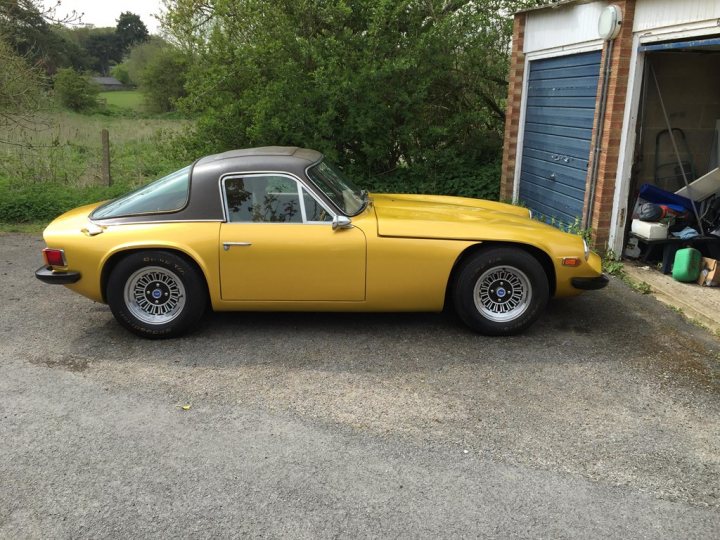 Early TVR Pictures - Page 90 - Classics - PistonHeads - The image features a vibrant yellow sports car parked in a driveway. The car is facing the camera and its shiny hood reflects the surroundings. The driveway is made of gravel, and there's a brick building with a white door partially visible in the background. A small section of lush green grass is visible on the left side of the frame. The overall scene suggests a quiet, suburban setting.