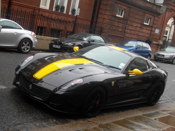 Rarities Spotted Supercars Pistonheads - The image depicts a street scene with a striking yellow Ferrari coupe parked on the side of the road. The car is sleek and polished, featuring the iconic Ferrari emblem and the "Scuderia Ferrari" badge on the hood. The car's side mirrors are positioned back as if someone has just parked it in a hurry.

Behind the Ferrari, there are several other cars parked along the street. The closest car is a black sedan, while a silver sports car and a blue minivan are slightly farther away.

The backdrop of the scene is an urban setting, with a building visible behind the group of parked cars. The ground appears wet, suggesting that it might have rained recently.

The photo seems to have been taken by a pedestrian, capturing the cars in an everyday city street scenario. The angle of the shot and the proximity to the Ferrari give the viewer a sense of its imposing presence in the street scene.