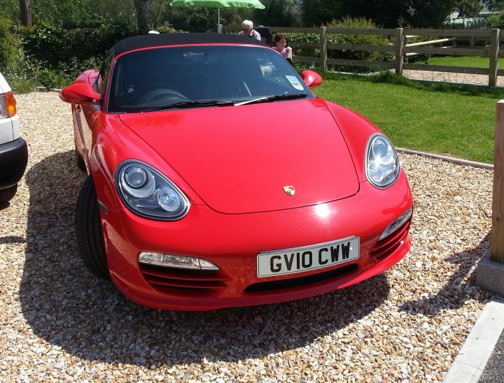 Wheel upgrade - Page 1 - Boxster/Cayman - PistonHeads - The image captures a vibrant red Porsche sports car parked on a gravel driveway. The car's gleaming exterior reflects the bright daylight, enhanced by the nearby objects. In the top left corner, the car is partially obscured by a white umbrella, suggesting that a sunny afternoon is in full swing. On the right side of the image, a wooden fence can be seen, adding a rustic charm to the scene. The car's license plate reads "GVI0 CWU", indicating its uniqueness. The combination of these elements paints a lively and picturesque setting.