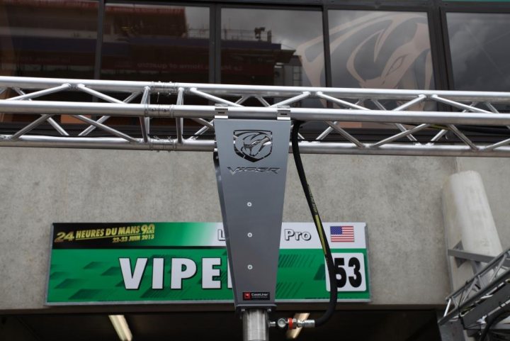 GT3-R - Page 1 - Vipers - PistonHeads - The image shows a large coiled black cord connected to a device with a small label that reads "Areca." The backdrop is a concrete wall with signs indicating various times and locations. These signs include "24 hues du mans," "PRO," and "53." The setting appears to be a racetrack or similar venue due to the design of the signs and the presence of the metal framework. The sky is visible through the windows in the background, indicating it might be late afternoon or early evening.