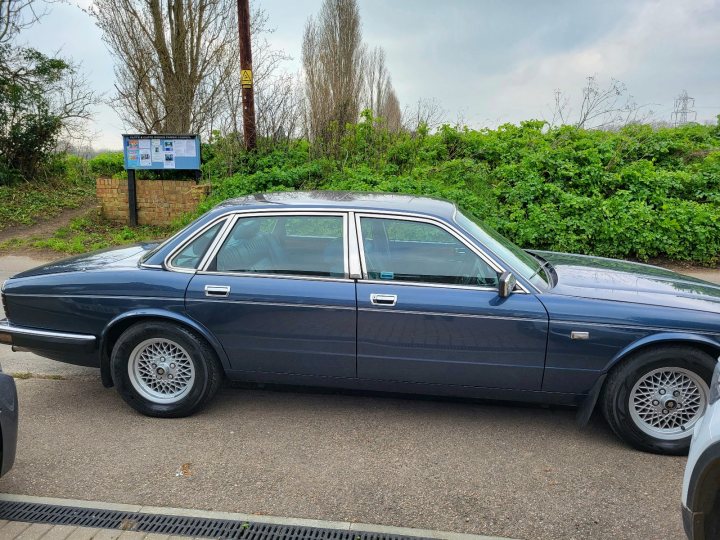 1988 Jaguar XJ40 Sovereign  - Page 1 - Readers' Cars - PistonHeads UK - The image showcases a dark blue vintage car parked in a lot. It's a classic model with chrome detailing, and the interior is visible through the windows. The car has white-wall tires and is positioned next to a building with signage, suggesting it might be a commercial or public area. The lot appears to be well-maintained, with pavement markings and no other vehicles in sight.