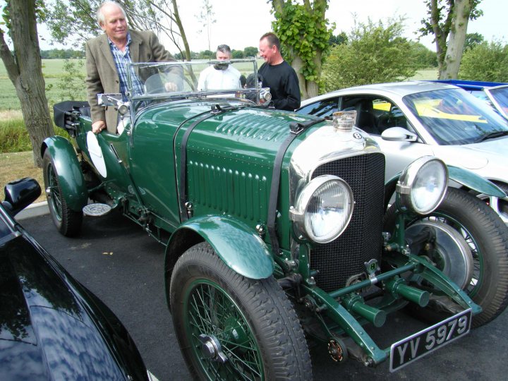 Breakfast Meeting, The Hare, Roxwell 4th June - Page 1 - Kent & Essex - PistonHeads - The image showcases a vintage green car, prominently positioned on the right side of the frame. This car, specifically a green Bentley, is parked alongside other cars, suggesting it's part of a collection or display. 

In the backdrop, there are a few trees and a second person, who appears to be the car's owner or a visitor admiring the antique. The vintage green car seems to be the center of attention, indicating it's likely a rare or unique vehicle. 

The creative and energetic atmosphere of the car show is depicted, with the presence of several other cars in the background. The Bentley's positioning and the crowd's attention suggest that it's a focal point of the event. 

The image encapsulates the allure of vintage cars and the inviting atmosphere of car shows, where people come together to share their passion for automobiles.