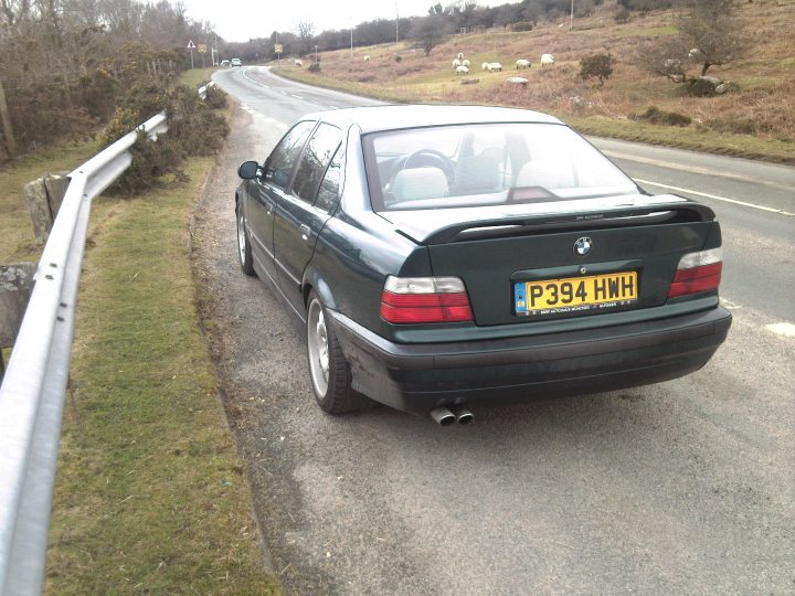 My 1997 E36 328i - Page 1 - Readers' Cars - PistonHeads - This image features a green BMW parked on the side of a winding country road. The BMW has the license plate "P394 HWH". The car is facing towards the left side of the photo, and its license plate is clearly visible. The road appears to be in a rural or semi-rural area, as there are sheep visible in the background. The car's position on the side of the road suggests it is either parked for a short period or waiting for traffic to come into view.