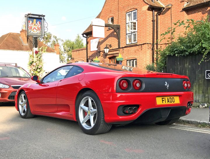 Shelby GT 500 outside the Baskerville in Shiplake - Page 2 - Thames Valley & Surrey - PistonHeads UK - The image shows a red Ferrari sports car parked on the side of a road. It's a bright and sunny day, as indicated by the clear sky above. A building with a brick wall can be seen in the background to the left. There are no people or significant actions visible in the frame. The car is positioned in the foreground, taking up most of the space, suggesting it might be the main subject of the image. The style of the photograph seems casual and unprofessional, with a slight angle and the car's position closer to the viewer than the surrounding environment.