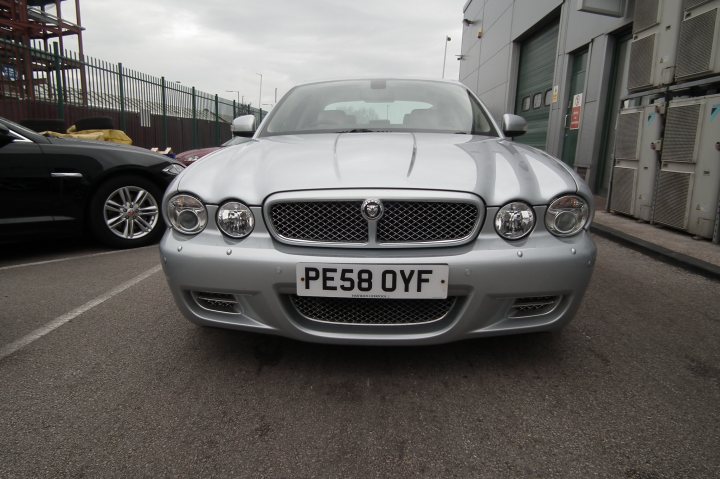 2009 XJR - Thoughts please  - Page 1 - Jaguar - PistonHeads - The image shows a silver luxury car parked on a gravel lot. The car has a sleek design with a prominent front grille and well-defined headlights. The license plate reads "PE58 OYF." In the background, there's a fence and a building, hinting at an industrial or commercial area. The weather appears overcast, with a mix of cloudiness in the sky.