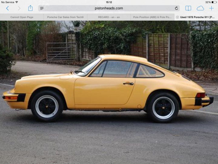 SC project - Page 1 - Porsche Classics - PistonHeads - The image shows an overhead view of a vintage yellow Porsche 914 on a road, viewed from the side. The car is parked outdoors, resting on a slight incline. The body of the car appears to be in good condition with a glossy paint job. In the background, there's a fence, greenery, and a gate. The car's distinctive shape, with its sloping hood and wide fender arches, is clearly visible and contributes to its distinctive look.