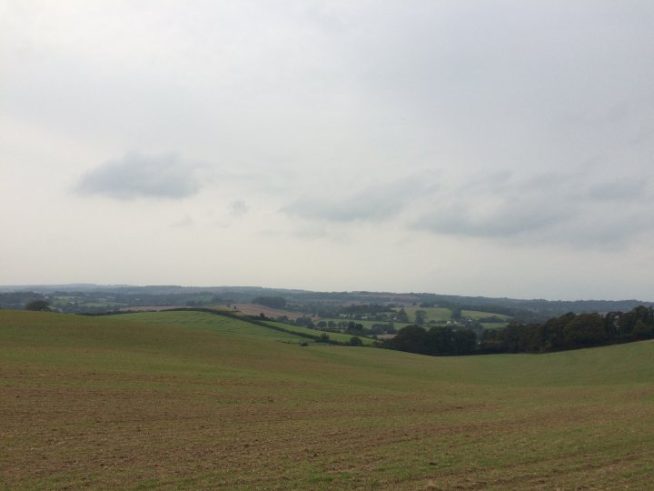 The "Photos From Today's Ride" thread... - Page 226 - Pedal Powered - PistonHeads - The image captures a serene landscape of a field. The sky is dotted with low, dark clouds, creating a dramatic backdrop. The field, showing signs of wear, is nestled between hills. The overall colors of the scene are muted, with the field appearing mostly green, moving into a landscape of multi-toned hills and walls in the distance. The relative positions of the elements in the image suggest a large open space, at the foot of a hill or at the center of a valley. The hills appear to be a significant part of the landscape, and their rolling contours provide a sense of depth and dimension to the scene.