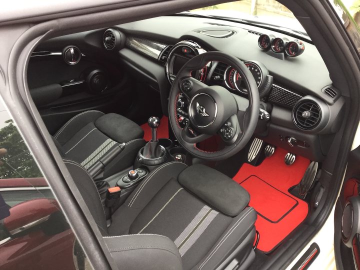 New JCW buyers  - thoughts so far ? - Page 1 - New MINIs - PistonHeads - The image provides an interior view of a car, specifically focusing on the driver's area. The dashboard, which is primarily black with a few accents in red, stands out in the image. The steering wheel is also black and positioned in the center of the dashboard. The driver's seat is visible, suggesting the condition of the vehicle's seating. The car also has a gear, which further indicates the model and type of vehicle. The back seat of the car is empty, leaving plenty of room for passengers. The red carpet on the passenger side adds a touch of color to the otherwise black interior.