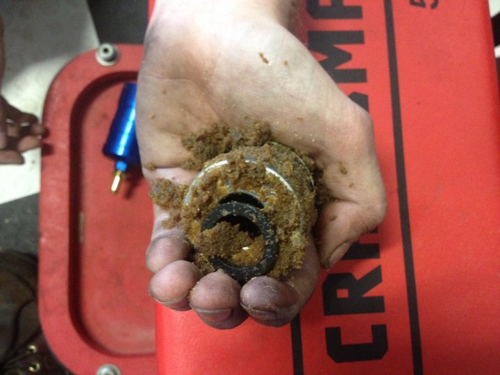 Fuel pickup problems on SR3 - Page 1 - Radical - PistonHeads - The image appears to depict a mechanical or artificial component, consisting of a cork seal and a metal ring, held by a human hand. The cork seal is dirty, with visible brown material, and the metal ring is also dirty with some black substance. The hand is resting on a red object, which could be a tool or piece of equipment, with a red handle featuring the word "CRIMSON" in white capital letters. The components seem worn and used, possibly from a disruptive woodworking operation known as "Crimson." The background suggests a mechanic's environment.