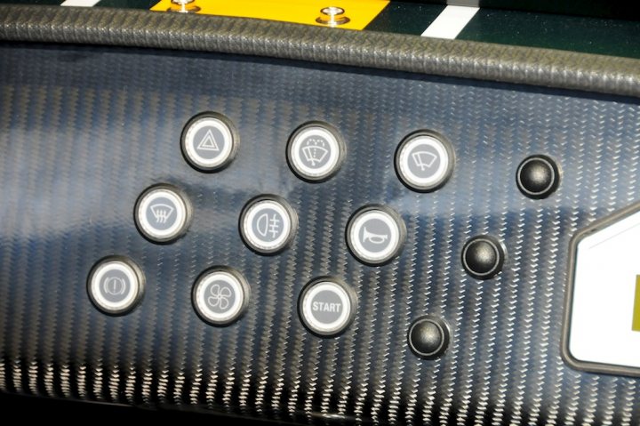 New Style Dash Switches on my R500 - Page 1 - Caterham - PistonHeads - The image shows a close-up view of a control console panel with multiple black circular buttons on a black background. The buttons are arranged in a grid-like pattern with varying symbols etched on them, indicating a variety of functions or selections. The panel exudes an air of a high-tech interface. In the background, there's a subtle glimpse of what appears to be a dashboard or a steering wheel, suggesting that the control console might be part of a vehicle. The overall design seems to be both user-friendly and aesthetically pleasing, with the black and white color scheme enhancing its appeal.