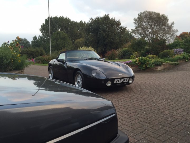 Random TVR pics - Page 425 - General TVR Stuff & Gossip - PistonHeads - The image depicts a quiet scene in a driveway. In the foreground, there is a classic black car with a distinctive round headlight, which suggests it's a vintage model. The car is parked diagonal to the camera, revealing the license plate that reads "243 JKN". The driveway where it is parked is neatly arranged with a mix of grassy areas and paved surfaces. In the background, behind a neat hedge, a variety of shrubs and trees can be seen, adding to the peacefulness of the setting.