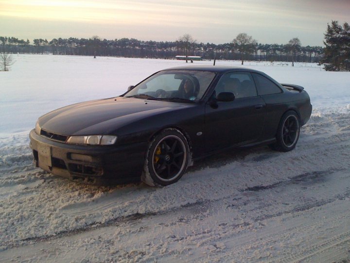 Pistonheads - In the image, a black sports car is parked on a snowy road, facing the viewer. The car's sleek design contrasts with the white, snow-covered ground. The car's rims are visible, and it appears to be parked by itself. The setting suggests it might be early morning or late afternoon given the soft light filtering through the overcast sky.