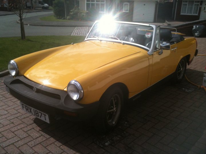 A car is parked in front of a parking meter - Pistonheads - The image features a yellow compact sports car, prominently parked on a brick driveway. The car is a two-door convertible model, as indicated by the visible soft top and a license plate reading "FR187T". The vehicle's classic design, evident in the soft angle of the roof and the overall shape, suggests it may be an older or vintage model. Behind the car, sunlight is visibly entering through the car's windows, creating a contrast with the exterior. To the right of the car, a garden area with a path and some hedges can be seen, adding a natural touch to the scene.