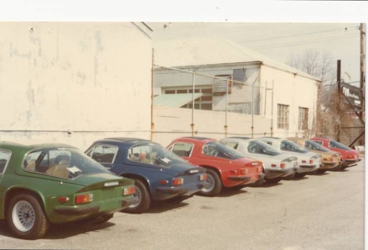 Last 3000S exports to US? - Page 1 - Classics - PistonHeads - The image shows a row of older, small cars lined up by a white building on an overcast day. The cars vary in design but share a retro aesthetic, suggesting they could be vintage models from the 1970s or 1980s. There is one visible person standing near the front car, suggesting some human presence at the scene. The cars are parked neatly in a row, with no other vehicles intruding the space between them. The buildings and the overall setting imply this could be a parking lot or a space designated to showcase these cars, possibly by a collector or a car enthusiast.