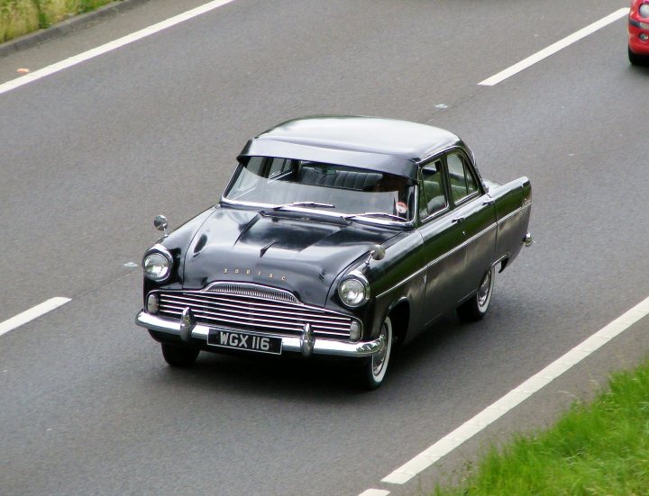 Herts, Beds, Bucks & Cambs Spotted - Page 332 - Herts, Beds, Bucks & Cambs - PistonHeads - This image captures a quaint scene on an open road. A vintage black car with silver trim is at the forefront, traveling down the right side of the road. The car's design is indicative of the 1950s, with traditional round headlights and a simple front grille. The car's license plate reads "MGX 16". The road is bordered by grass on the left, suggesting a rural or semi-rural setting.