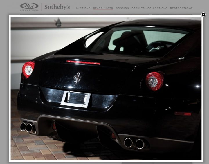 Manual Ferrari 599 at auction - Page 1 - Ferrari V12 - PistonHeads - The image depicts the rear of a luxury car displayed in a showroom. The car is black and features distinctive red brake lights. It prominently showcases chrome exhaust tips at the rear. The display setting includes a tiled floor and a white wall in the background. The car's sleek design and details suggest that it is a high-end model.