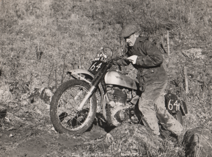 Tribute To A Racer - Page 1 - Classic Cars and Yesterday's Heroes - PistonHeads - This is a black and white photo that captures a dramatic moment of dirt bike racing. A man, presumably the rider of the motorcycle, is leaning forward in a dynamic pose, as if maneuvering the bike through difficult terrain. The motorcycle is numbered, indicating it's part of an organized racing event. The backdrop is a natural landscape, with trees and rocks, suggesting the race is taking place off-road.