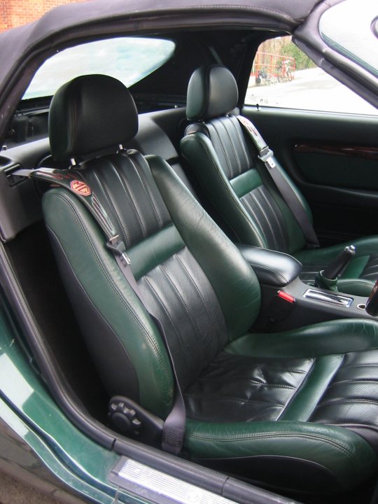 Bargain Pistonheads Mgf Exist - The image shows the driver's side interior of a car. The car's upholstery is luxurious, featuring green leather seats that appear new and well-maintained. The steering wheel is positioned on the right side of the car, which suggests that this vehicle is manufactured for driving on the left side of the road. The dashboard is visible, and there's a passenger side mirror installed, which suggests that the mirror is foldable when not in use. The car appears to be stationary, given the orientation and lack of motion blur in the image.