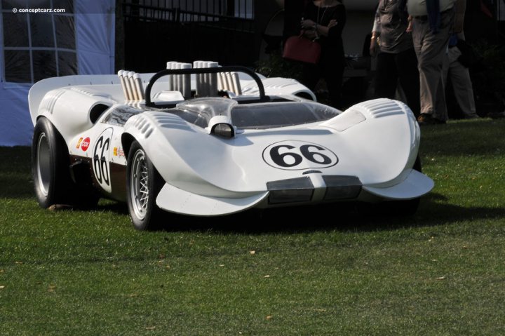 CPOP 2015       What are YOU looking forward to? - Page 1 - Cholmondeley Power and Speed - PistonHeads - In the image, a striking white car with a large, open nose and a sleek, pointed tail visits a sunny outdoor event. The car's black hood contrasts with its white body, and it features cool-looking details like round headlights and a prominent "66" on the side. A crowd of people, including an individual standing in the background, gather around the car, admiring its unique features. The car is parked on a patch of lush green grass, casting a slight shadow behind it, indicating the presence of sunlight, possibly suggesting an outdoor setting for this gathering.