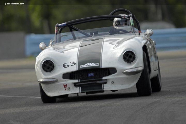 Early TVR Pictures - Page 72 - Classics - PistonHeads - The image captures a vintage race car in motion, driving on a track. The car, which has the number 63 displayed on it, has a sleek silver body and a distinctive black stripe running along the side. A single headlight on the front suggests an older model design. The background is blurred, emphasizing the speed and the dynamic nature of the race.