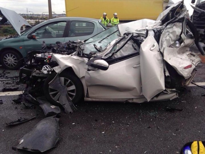 Heads up Avoid Dartford Crossing today - Page 1 - Kent & Essex - PistonHeads - The image shows a severe car accident with two vehicles - a silver car and a green car. The silver car has been crushed extensively with its side crumpled and the hood crushed inwards. The green car appears to be also severely damaged with its side, front, and hood compromised. The incident appears to have been violent with significant vehicle damage. Visible in the background are people who might be contemplating the destruction or possibly handling the situation. The sky is overcast, adding a somber tone to the scene.