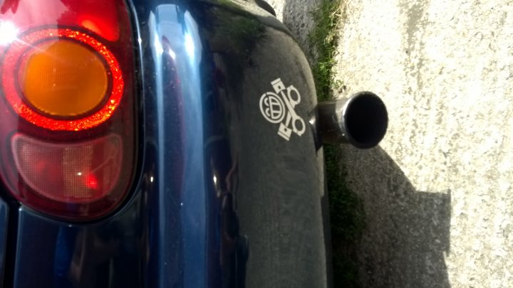 A red fire hydrant sitting on the side of a road - Pistonheads - The image showcases a blue car parked on a concrete surface. The car's tailpipe, visible on the right side of the image, is noteworthy for its black color and a unique design featuring three white circles. These three circles are placed in a descending order, creating a distinct visual contrast to the surrounding black color. The car's brake light, located on the left side of the image, appears to be illuminated, possibly indicating a stop or slow-down command by the driver. The concrete surface and the absence of any distinct background elements suggest that the focus of the image is on the car's tailpipe and brake light.