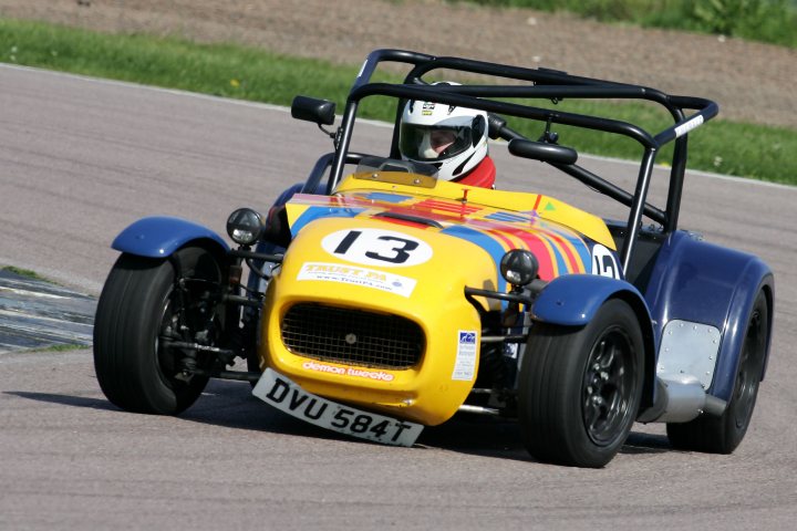 Importing a Westfield minus engine/box - Page 1 - Australia - PistonHeads - The image depicts a race scene with a person driving a quirky, brightly colored car bearing the number 13. The car is uniquely designed with a blue roof and yellow body, giving it a vibrant and eye-catching appearance. The driver, donned in safety gear including a helmet, is focused on the track. The background reveals a racetrack with a blurred view of the surroundings, suggesting that the vehicle is in motion. The car's design and vibrant colors set it apart in the competitive environment of the race track.