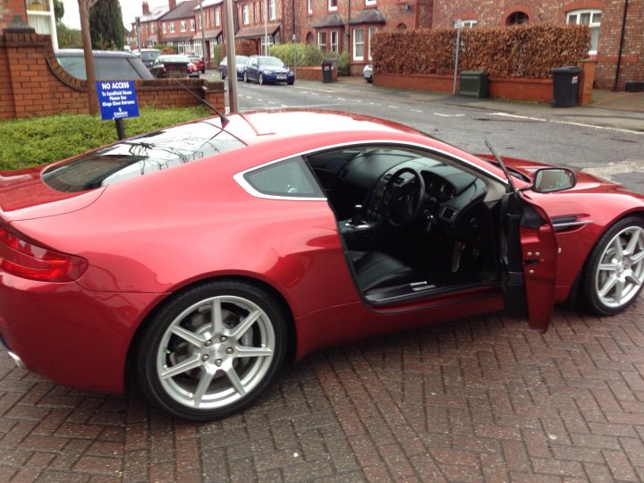 A red car is parked on the side of the road - Pistonheads - This image shows a red sports car parked on a brick driveway. The car's door is open, providing a clear view of the dark interior. Adjacent to the driveway, there's a sign that reads "No Driveway Obstruction," indicating that the street is public and does not belong to a driveway. In the background, there are residential buildings and parked cars, suggesting a suburban setting. The sky is overcast, indicating cloudy weather.