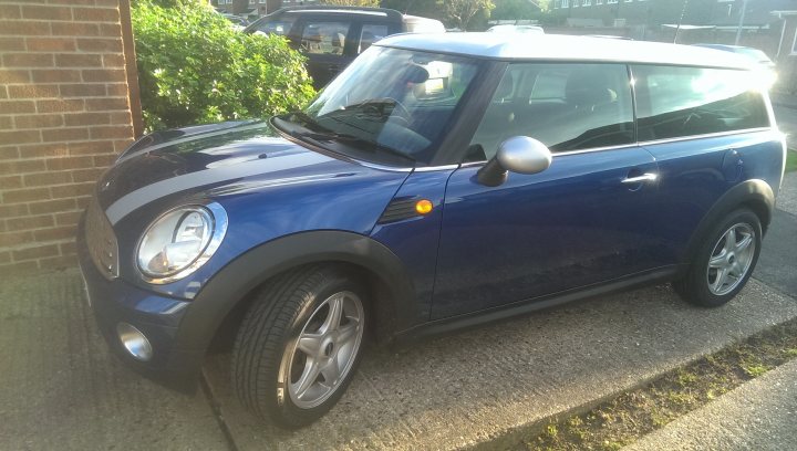 Scoob is dead, long live the mini (sort of) - Page 1 - East Anglia - PistonHeads - The image shows a compact car parked on a concrete driveway. The car is a dark blue color and appears to be a Mini Cooper. Its body is in good condition, and it has a shiny finish. There are no visible scratches or dents. The car is parked next to a garden area where a few plants and flowers are visible. The sunlight is shining from the right side of the image, casting a warm glow on the car and brightening the scene.