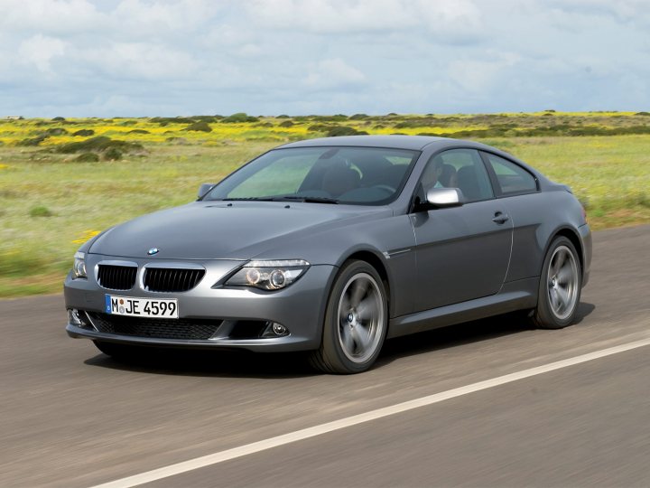 Old v New - Page 1 - Classic Cars and Yesterday's Heroes - PistonHeads - The image shows a silver BMW Coupe car driving on a road with a horizon of open fields. The car has a distinctive license plate that reads "M-JE4599," and it's positioned diagonally across the frame from the bottom left to the top right, giving a sense of motion. The setting suggests a rural or semi-rural landscape, and the sky appears clear with ample daylight illuminating the scene.