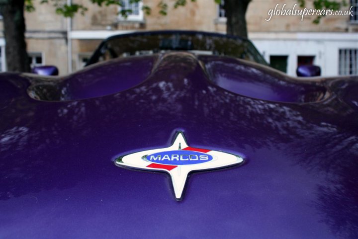 Sunday April 25th Bradford on Avon - Marocs - Page 1 - South West - PistonHeads - The image features the hood of a car, specifically a Marcos, which stands out due to its purple hood. The car is parked by a tree, and the padding on the hood appears to be slightly worn, adding character to the vehicle. The Marcos logo is prominently displayed in the center of the hood. The hood seems to be missing a part, possibly a cover, which adds a touch of intrigue to the image.