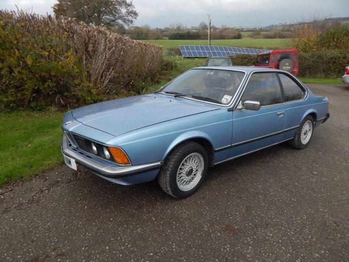 Classic (old, retro) cars for sale £0-5k - Page 50 - General Gassing - PistonHeads - The image shows a blue car parked in a lot. The car is positioned facing towards the left side of the frame, and the focus of the photo is primarily on the front of the vehicle. The car appears to be small or compact in size, as judged by its front end and the visible lines indicating the shape of its doors. A solar panel is affixed to the top of the car, suggesting that the vehicle may be equipped with a renewable energy source. The background of the image consists of various elements such as foliage, grass, and a red truck parked farther away. The photo is taken during the day under cloudy skies.