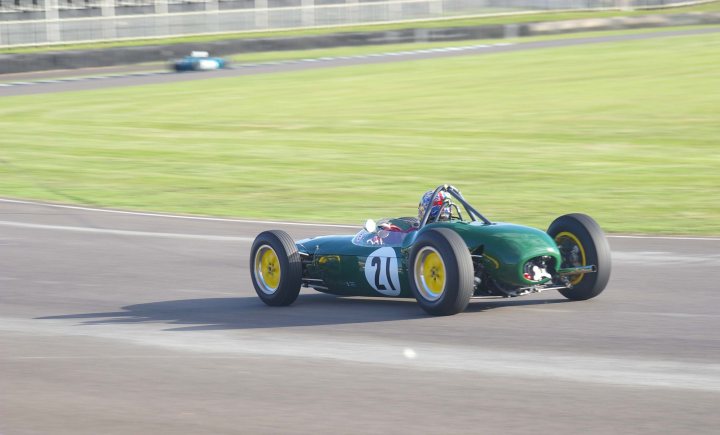 2012 Goodwood Revival Meeting Photo Gallery - Page 1 - Goodwood Events - PistonHeads - The image shows a vintage race car driving on a track. The car has a predominantly green color scheme and is adorned with yellow detailing, which could be logos. Its design is reminiscent of 1960s racing cars, and it is seen during the daytime under clear skies. The car's number is visible, which is 17, but specific driver information is not provided. The background scene features a blurred fence and grass, suggesting high speed and providing a sense of motion and setting.