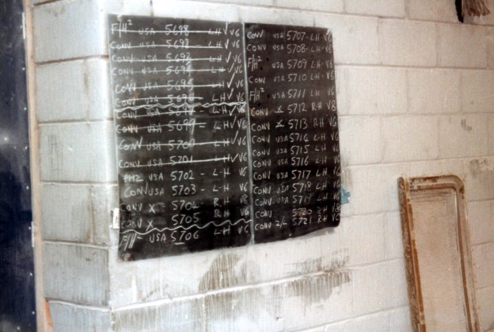 Ooh Gonna Pistonheads - The image shows a white brick wall with a piece of paper or cloth hung on it featuring a list of numbers and letters written in chalk. The text on the wall is handwritten and likely signifies some form of pricing or purchasing information. The style of the handwriting varies in size and emphasis, suggesting that it might have been added over time or by multiple people. The overall scene appears to be quite old and possibly located in a place where such handwritten information was commonly used. The aged look of the wall and the soiled appearance of the paper indicate that the writing has been in place for quite some time, weathering the effects of time and use.