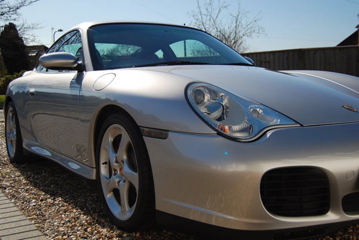 Pistonheads - The image shows a silver Porsche sports car parked on a gravel driveway. The car is positioned at an angle, displaying the back of its front wheel and the side of its side wheel. The design of the car is sleek and sporty, with the Porsche emblem prominently visible on the front side. The car appears to be in very good condition, suggesting it's well-maintained. There's a tree visible in the background, adding a natural element to the otherwise man-made scene.