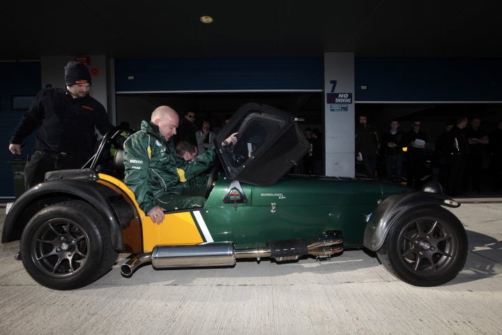 Some Pictures of my R500 Signed - Page 1 - Caterham - PistonHeads - In this image, a man is seated inside a vintage green and gold sports car, which is situated in an underground parking garage. The car has its hood propped open, and the you can see various mechanical components inside the engine bay. The man appears to be examining or possibly performing maintenance on the vehicle. In the background, several other cars are parked, and other individuals are present, though they do not seem to be related to the car in the foreground. The lighting in the image is artificial, contributing to a somewhat moody ambiance.